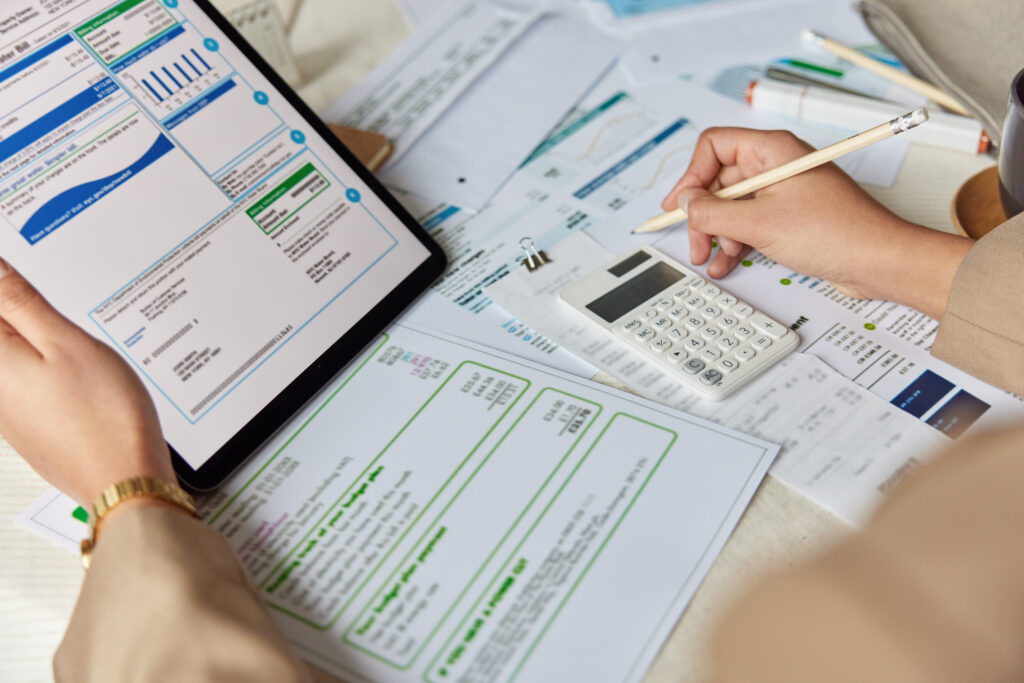 Unrecognizable Female Worker Counts Budget On Calculator Reviews Receipts And Bills Finds Profit Makes Notes With Pencil Checks Information On Digital Tablet Makes Audit Of Bookkeeping Entries